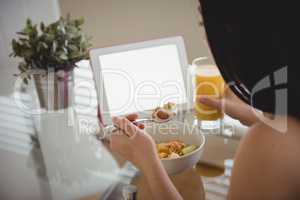 Woman eating breakfast while using laptop