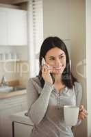 Smiling woman talking on mobile phone while holding coffee mug