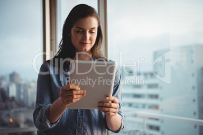 Smiling woman holding digital tablet while standing by window