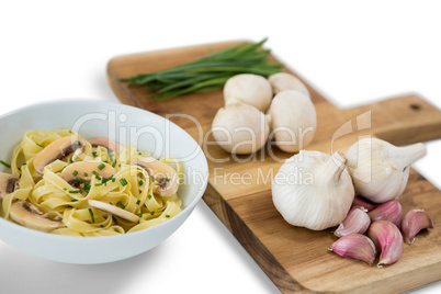 Close up of vegetables with garlic on cutting board by pasta in bowl