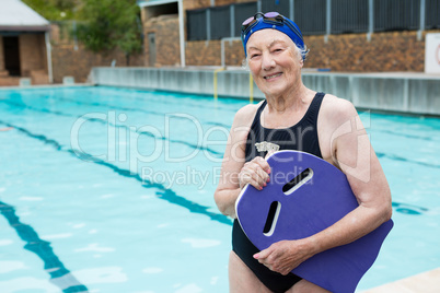 Smiling senior woman holding kickboard at poolside