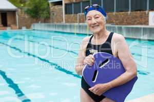 Smiling senior woman holding kickboard at poolside