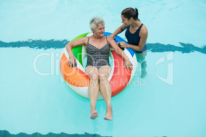 Trainer assisting senior woman on inflatable ring in swimming pool