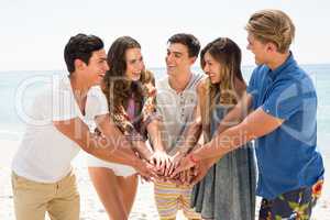 Smiling friends stacking hands at beach