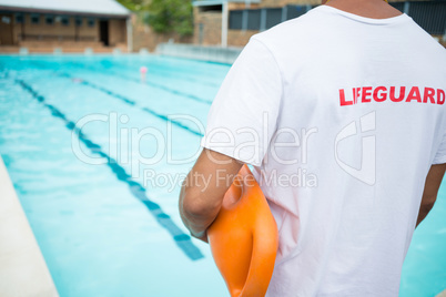 Lifeguard standing with rescue buoy near poolside