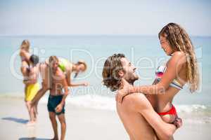 Smiling young man lifting woman at beach