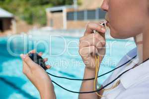 Female coach blowing whistle and looking at stopwatch