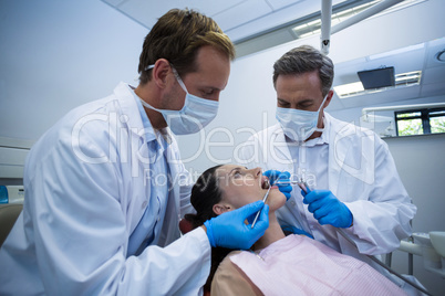 Dentists examining a female patient with tools