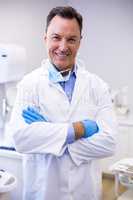 Smiling dentist standing with arms crossed at dental clinic