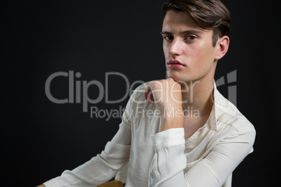 Androgynous man sitting on chair with hand on his chin