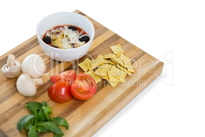 Cooked food in bowl by ravioli and vegetables on cutting board