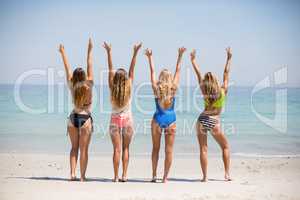 Female friends in bikinis with arms raised at beach