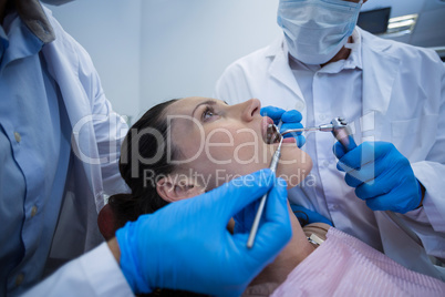Dentists examining a female patient with tools
