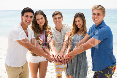 Friends stacking hands while standing at beach