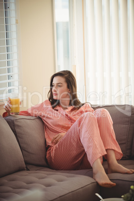 Woman holding juice while sitting on sofa