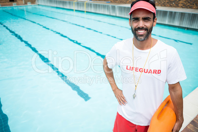 Lifeguard standing with rescue buoy near poolside