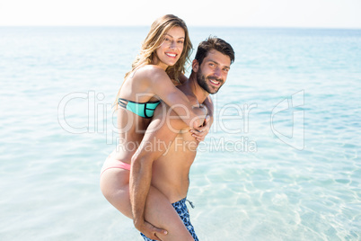 Young man piggybacking girlfriend on shore at beach