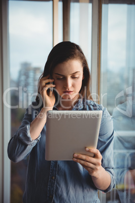 Woman talking on mobile while looking at tablet