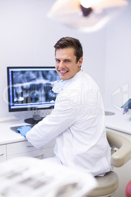 Portrait of happy dentist examining x-ray report on computer