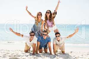 Friends forming pyramid with arms raised at beach