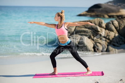 Young woman practicing warrior pose at beach