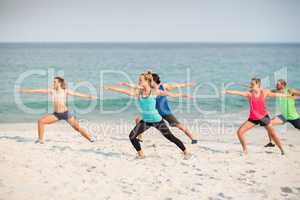 Friends practicing warrior 2 pose on shore at beach