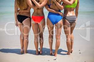 Low section of female friends in bikinis at beach