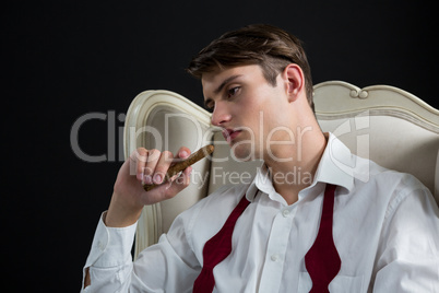 Thoughtful androgynous man sitting on chair with cigar