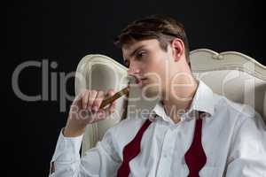 Thoughtful androgynous man sitting on chair with cigar