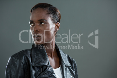 Androgynous man in black jacket posing against grey background