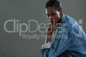 Androgynous man in denim jacket posing against grey background