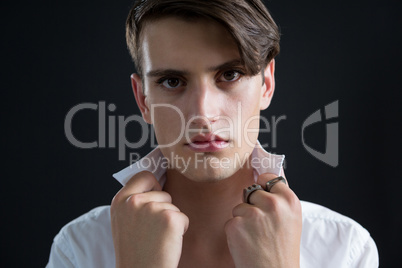 Androgynous man holding his collar against black background