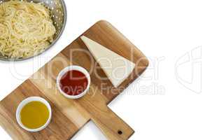 Pasta in colander by sauce and cheese on cutting board