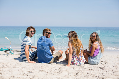 Cheerful friends sitting on shore during sunny day