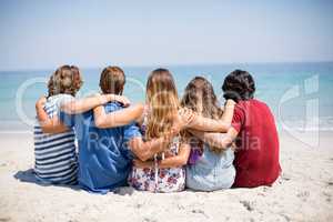 Friends sitting with arms around at beach