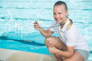 Portrait of swim coach holding stopwatch and showing thumbs up at poolside