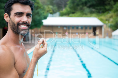 Smiling lifeguard standing with whistle near poolside