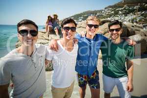 Male friends standing at beach during sunny day