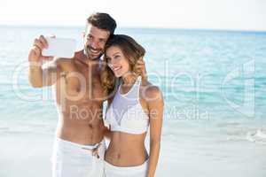 Couple taking selfie while standing on shore at beach