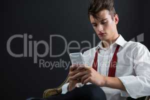 Androgynous man sitting on chair and using mobile phone