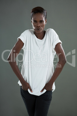 Androgynous man posing with hands in pockets against grey background