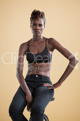 Androgynous person sitting on stool against beige background