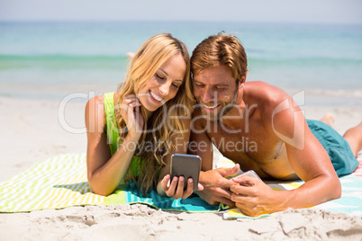 Couple looking in mobile phone while lying at beach