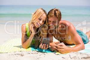 Couple looking in mobile phone while lying at beach