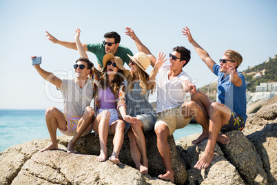 Friends taking selfie while sitting on rock formation at beach