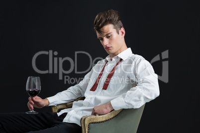 Thoughtful androgynous man sitting on chair with glass of wine