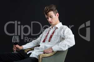 Thoughtful androgynous man sitting on chair with glass of wine