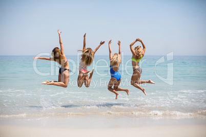 Female friends in bikinis jumping on shore
