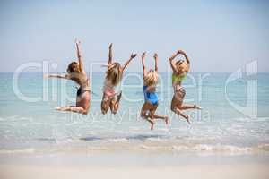 Female friends in bikinis jumping on shore