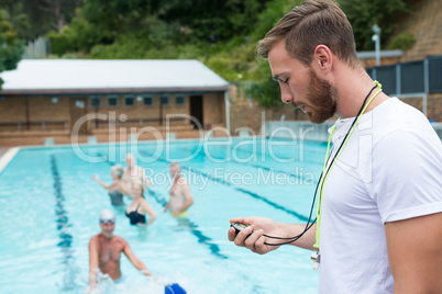 Swim coach looking at stopwatch near poolside